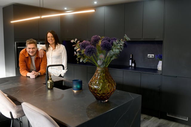 Tom and Amanda Cook in the kitchen. The kitchen cabinetry and the island are from Howdens, a supplier Amanda uses for her commercial design work. The units are in matt black and the worktop, island top and splashbacks are in durable Dekton from Consentino. The island is also home to a “deck drawer” and disco lights which keen DJ Tom takes charge of when the Cooks want to get the party started.