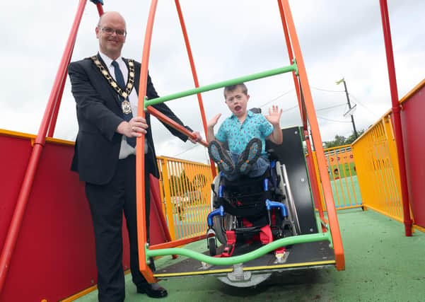 Mayor of Antrim and Newtownabbey, Cllr Jim Montgomery with local resident Luke Mullan enjoying the wheelchair accessible swing at Antrim Lough Shore play park.
