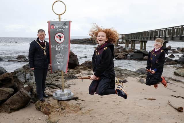 Mayor of Causeway Coast and Glens Borough Council, Alderman Mark Fielding accepts decorative banner in an official ceremony at Ballycastle Beach, honouring Ballycastle's role in the Harry Potter
companion book, Quidditch Through The Ages Illustrated Edition with art by Emily Gravett,
available in hardback from 6th October.

Pictured with Cross and Passion College pupils Aine (11) and Oisin Franey (9).