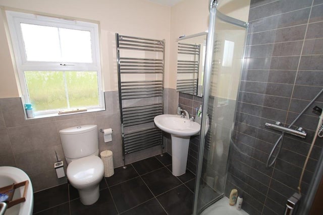 The modern family bathroom has tiled floor and part walls, freestanding bath with chrome feet, WC, wash hand basin, corner shower, spotlights, lighted mirrored cabinet and a heated towel rail.
