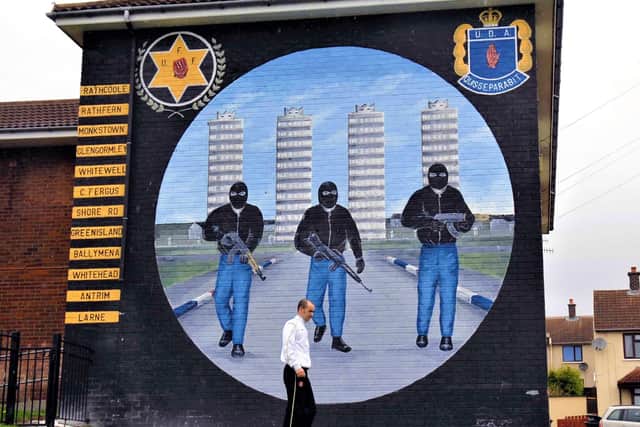 A man walks past a UDA South East Antrim brigade mural in Rathcoole, listing the group's local 'battalions'