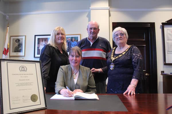 Family members Amanda Steede, Joe Steede, and the Mid and East Antrim Deputy Mayor Beth Adger MBE watch on as Elizabeth Steede signs the visitor's book in the Mayor's Parlour