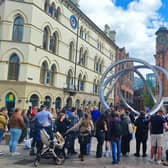 A street entertainer holds the attention of a crowd at Cornmarket in the centre of Belfast on a sunny day with occasional cloud.