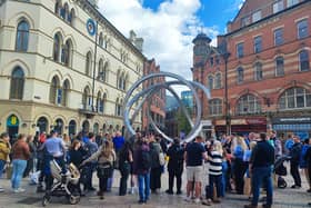A street entertainer holds the attention of a crowd at Cornmarket in the centre of Belfast on a sunny day with occasional cloud.
