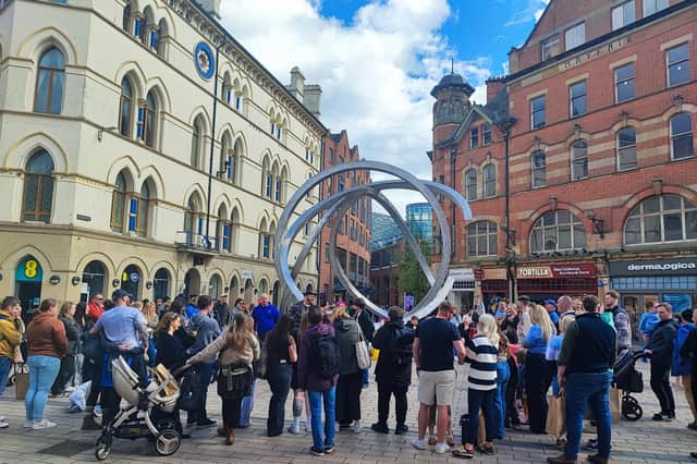 A street entertainer holds the attention of a crowd at Cornmarket in the centre of Belfast on a sunny day with occasional cloud.