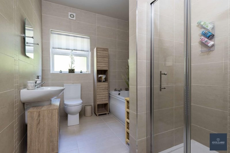 The contemporary white four-piece family bathroom features a walk-in shower cubicle with Triton electric shower, panel bath, sink with vanity unit below, dual flush WC and a heated towel rail. There are also fully tiled flooring and walls.
