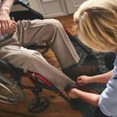 Female healthcare worker helping disabled senior man in wheelchair, tie shoe laces. Credit: Getty Images