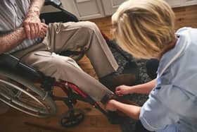 Female healthcare worker helping disabled senior man in wheelchair, tie shoe laces. Credit: Getty Images