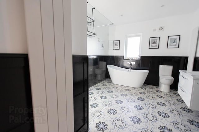 The spacious bathroom features a bath,  low flush WC, vanity unit, a fully tiled floor, partially tiled walls, a walk-in shower and has wood panelling on the walls. There is also an airing cupboard.