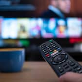Netflix remote control with TV behind in evening with Netflix menu (Shutterstock)