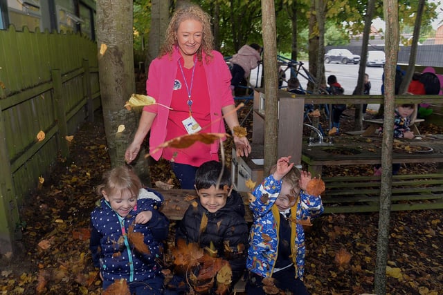 Nursery assistant at Portadown Integrated Primary School Nursery Unit Ann-Marie Cullen playing with fallen leaves with pupils from left, Harper, Vihaan and Devan. PT42-313.