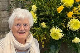 Pat Crossley pictured beside a floral arrangement depicting the RNLI colours in Westminister Abbey celebrating 200 years of saving lives at sea