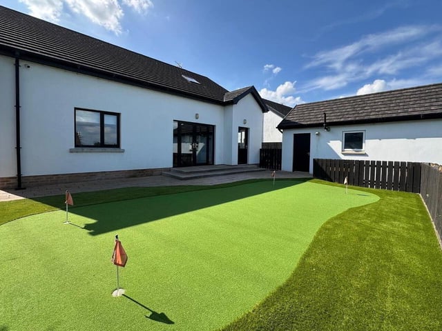The fully-enclosed rear garden featuring an artificial grass putting green, perfect for golf enthusiasts.