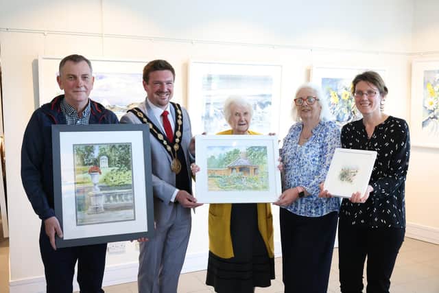 Lisburn resident Marion Hiddleston took first place in the competition for her colourful depiction of the summer house, located within the walled gardens of Rowallane Gardens. 
The second and third places were taken respectively by Lawrence Chambers for his detailed depiction of Lady Alice’s Temple in Hillsborough Castle Gardens and Helen Sara McLarnon for her interpretation of the gardens surrounding Hillsborough Castle. The artists are pictured with then Mayor Scott Carson and Councillor Hazel Legge