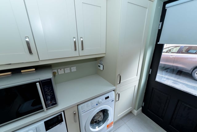 Utility room with range of fitted high and low level units, tiled floor, and door to rear garden.