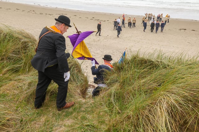Orange men and women make their way through the dunes to the beach