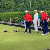 Lurgan bowlers discussing the head situation and Nigel Hamilton bowling in the background