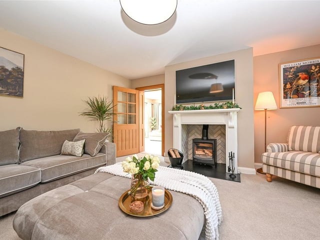 Reception room with luxury carpet flooring and wood-burning stove set on a slate hearth with a herringbone brick feature backdrop and painted oak surround.