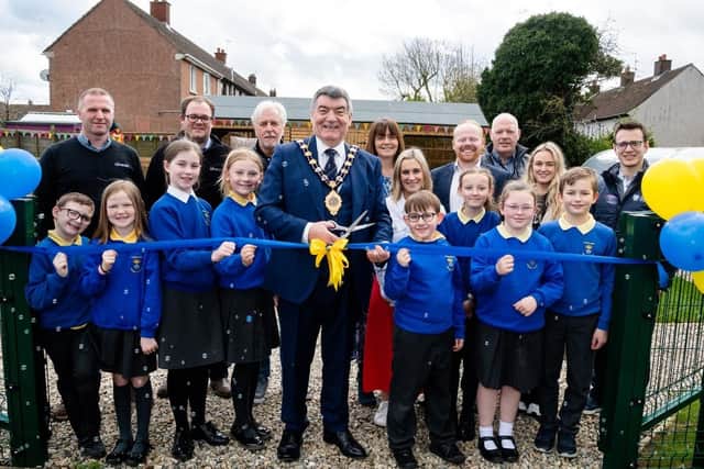 The outgoing Mayor of East and Mid Antrim, Noel Williams, cuts the ribbon to open Sunnylands Primary School's growing space. Included are pupils, staff from the Housing Executive and Idverde and elected representatives.