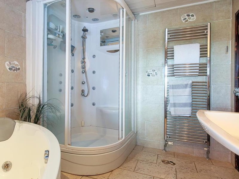 Bathroom with contemporary white four piece suite comprising whirlpool style corner bath, separate steam shower cabin with body jet system, pedestal wash hand basin and WC.