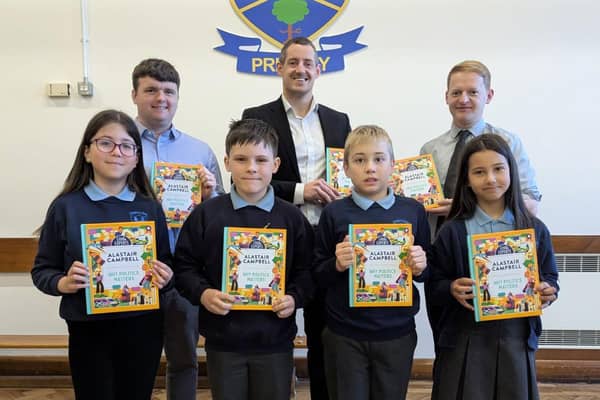 Pinsent Masons’ Senior Associate Matthew McMurray (back row, centre) presents copies of Alastair Campbell’s ‘Why Politics Matters’ book to pupils at Dunclug Primary School. They are joined by school principal Alastair Beacom (R) and teacher Scott Marcus. CREDIT OSCNI