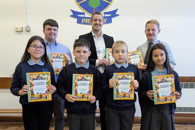 Pinsent Masons’ Senior Associate Matthew McMurray (back row, centre) presents copies of Alastair Campbell’s ‘Why Politics Matters’ book to pupils at Dunclug Primary School. They are joined by school principal Alastair Beacom (R) and teacher Scott Marcus. CREDIT OSCNI