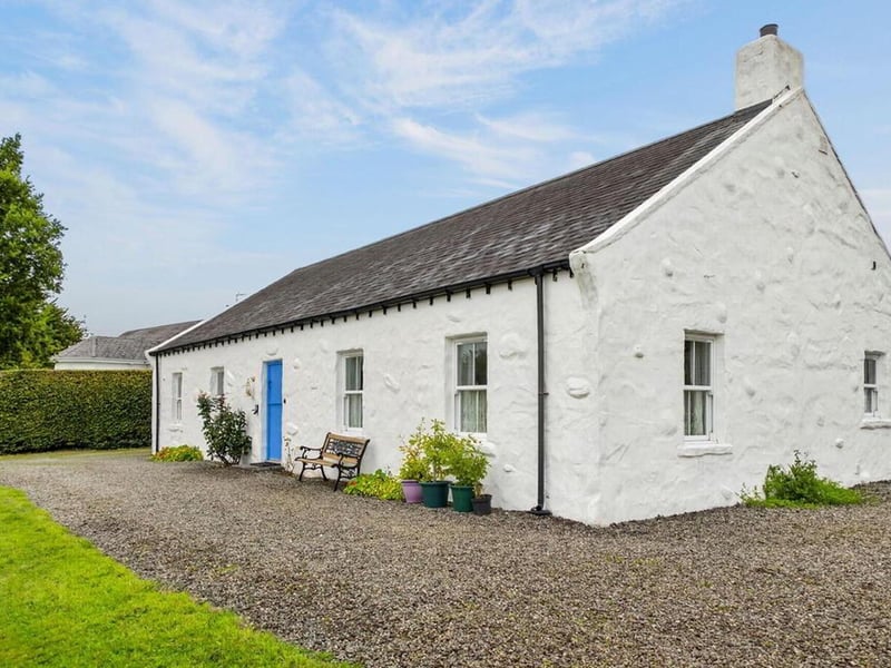 Constructed approximately 15 years ago to a high specification, this distinctive property has been thoughtfully designed and built using carefully selected reclaimed materials and traditional architectural features, creating the character and atmosphere of a much older country cottage whilst offering the benefits of a modern home. The four-bedroom property is characterised by its traditional whitewashed exterior, natural slate-style roof, charming blue entrance door and attractive timber detailing. Internally, the accommodation continues the cottage theme with textured plaster finishes, timber-panelled ceilings, natural wood flooring, traditional pine kitchen cabinetry, a feature range-style cooker and an elegant freestanding roll-top bath. Occupying a spacious site extending to approximately 0.25 acres, it also benefits from attractive gardens, generous gravelled parking and courtyard areas, together with a detached garage constructed in a style sympathetic to the main residence. It's on the market for a guide price of £345,000 with Mid Ulster Homes.