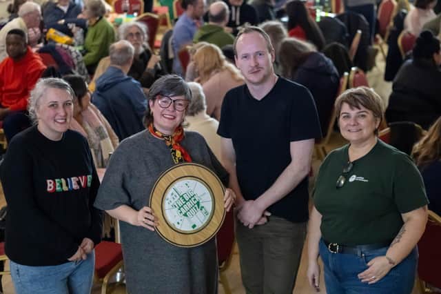 Lisa, Lee, and Lynn of Positive Carrickfergus, joined by Bill Buchanan from Deja Vu Promotions, display The Big Carrick Quiz Shield before passing it on to the deserving winner.