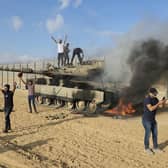 Palestinians celebrate by a destroyed Israeli tank at the Gaza Strip fence east of Khan Younis Saturday, Oct. 7, 2023. The militant Hamas rulers of the Gaza Strip carried out an unprecedented, multi-front attack on Israel at daybreak Saturday, firing thousands of rockets as dozens of Hamas fighters infiltrated the heavily fortified border in several locations by air, land, and sea and catching the country off-guard on a major holiday (AP Photo/Hassan Eslaiah)