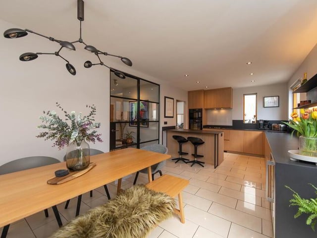 Kitchen with built in units, luxury work surfaces and matching splash back, incorporating a single drainer with mixer taps, inlaid gas hob unit, double oven, built in fridge and display shelving, dishwasher, breakfast bar, extractor fan, and luxury floor tiling.