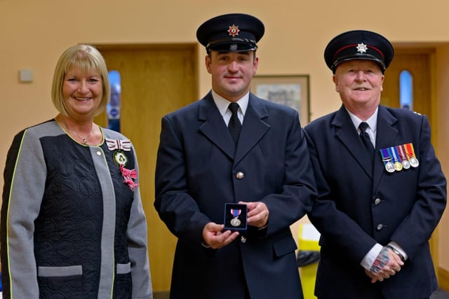Firefighter Andrew Doey with the Deputy Lieutenant for Co Antrim, Mrs Jackie Stewart MBE, and Watch Commander Brian Smith.