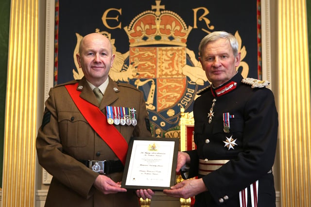 Colour Sergeant Mark Kitchen was praised for ‘selfless commitment, dedication to service and unwavering devotion to duty’ over a Reserve career spanning more than 30 years.
During his career he has attended every one of his unit’s annual deployment exercises, stepping up to the challenge of acting as Team Leader at the 2012 Olympics in London.
Prior to and throughout Op SHAMROCK BRIDGE (the funeral of her Late Majesty Queen Elizabeth) Col Sgt Kitchen demonstrated his unparalleled value to the Battalion and the wider Army Reserve.  The Citation paid tribute to Colour Sergeant Kitchen’s ‘forward planning, efficiency and pragmatism’, adding ‘Quite simply, Colour Sergeant Kitchen was the linchpin in a detailed logistics plan and delivered it  superbly, attracting widespread praise and recognition across civic, political and military circles within Northern Ireland’.
Colour Sergeant Kitchen is also an integral member of his battalion’s Bugle Section in which capacity he has performed at a vast range of events and was a key player within the Bugles, Pipes & Drums Queen’s Platinum Jubilee Celebrations across the UK.
Colour Sergeant Mark Kitchen is pictured receiving The Lord Lieutenant’s Certificate for Outstanding Meritorious Service Above and Beyond The Call of Duty from Mr David McCorkell, His Majesty’s Lord Lieutenant for the County of Antrim.