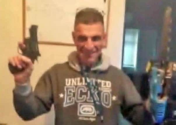 A grinning William McFall from Greenisland posing with a pistol and chainsaw in an image found on a mobile phone seized by police.