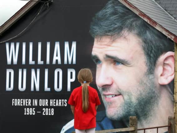 A banner in memory of William Dunlop has been erected in Armoy ahead of the Irish road race meeting next weekend. Six-year-old Ellie McAuley from Armoy looks on at the tribute, which is in the race paddock.