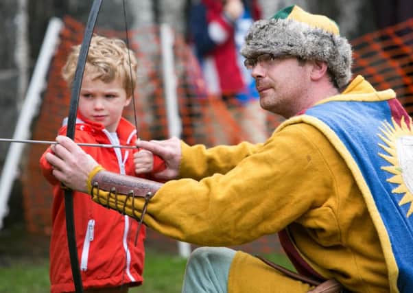 Three-year-old Lucas Dowling from Belfast tries his hand at archery under the supervision of archer Shane McAllister during the longbow display at Carrick Castle on Monday. INCT 22-482-RM