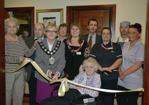 Mayor of Ballymena Councillor Audrey Wales is assisted by Kintullagh Nursing Home residents Lena McLaughlin and Ethel Warnock as they cut a ribbon to mark the official opening of  the Yellow Rose Cafe a place where patients can be join by relatives and friends for morning coffee or afternoon tea. Also included are staff, fellow residents and home manger Jane Moore . INBT 50-117JC