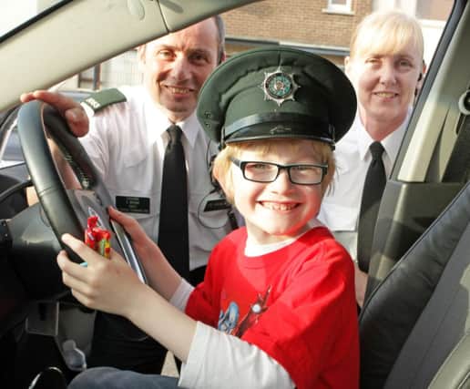 IF THE CAP FITS. Young Lewis is certainly in the driving seat as he was pictured in a PSNI car on Friday night at the Leaney PS Summer Fair along with PSNI members Davy and Anna.INBM23-14 035SC.
