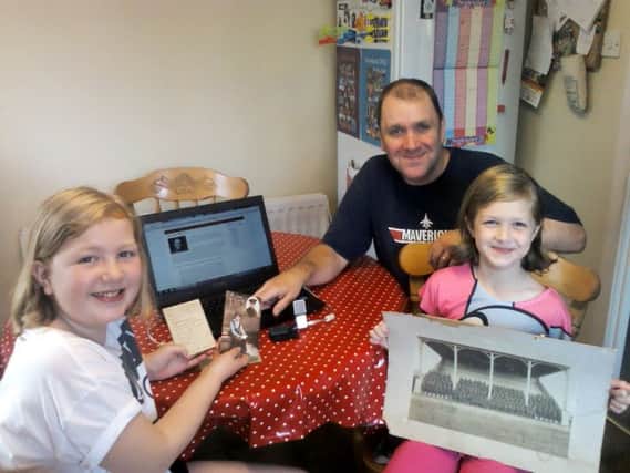 Mark and his daughters Charlotte (10) and Katherine (8) pictured with a photo of grandfather John Adams snr in a Battalion and some field cards. Also the johnadams.org.uk/letters website is pictured on the computer with the podcasting mic on the table. Inbm38-14s