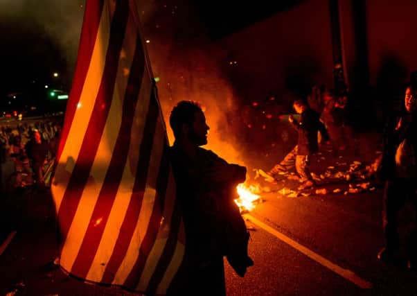 James Cartmill holds an American flag while protesting in Oakland, Calif., on Monday, Nov. 24, 2014, after the announcement that a grand jury decided not to indict Ferguson police officer Darren Wilson in the fatal shooting of Michael Brown, an unarmed 18-year-old. Several thousand protesters marched through Oakland with some shutting down freeways, looting, burning garbage and smashing windows. (AP Photo/Noah Berger)
