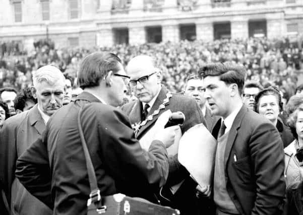 1965... With a dense crowd in the background, Derry Mayor AW Anderson (centre), Mr. Eddie McAteer MP and John Hume, chairman of the University for Derry committee, are interviewed on the steps of Stormont after thousands of local people travelled to Parliament Buildings to protest at a decision to locate a new university in Coleraine and not Derry. [21-05-12 SML 32]