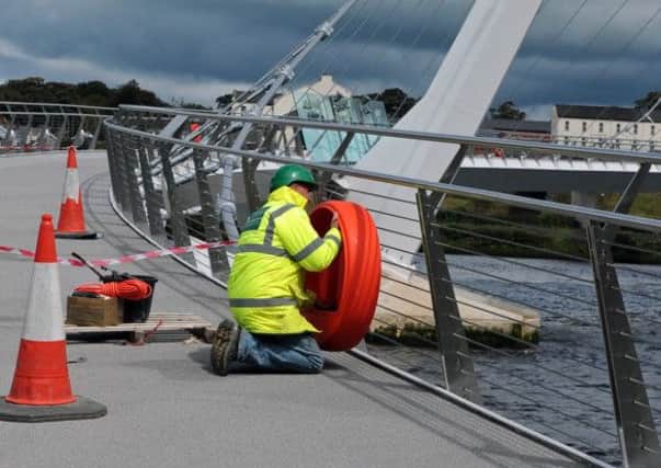 A workman placing the housing for a lifebelt on the railings of the Peace Bridge