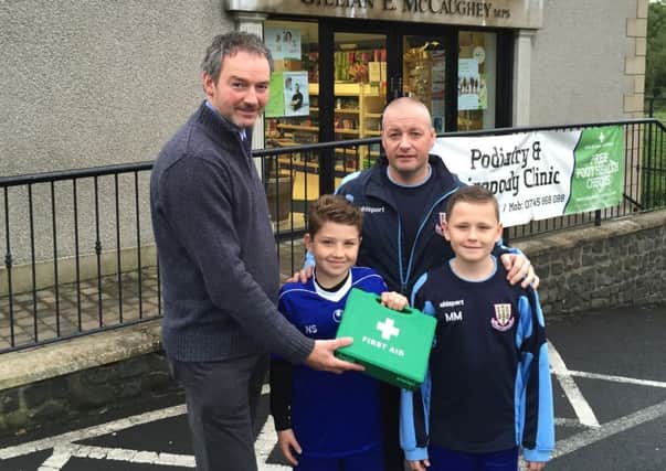 William McCaughey, from Kells & Connor Pharmacy, presents a first aid kit for Ballymena United under-11s to players Noah Scullion and Mark McClean and coach John McClean.