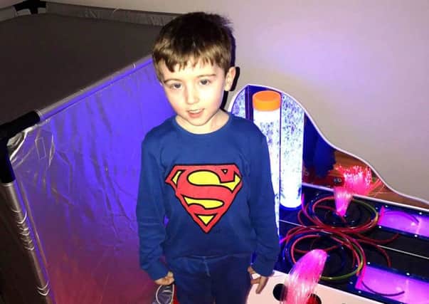 Jacob Blayney dressed as Superman, stands in front of his dark den, bubble tube and fibre optic lighting.