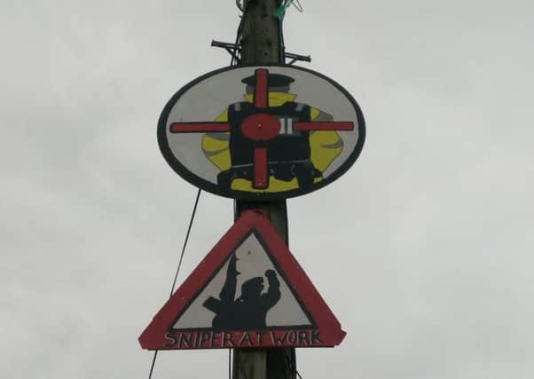 A sign depicting a target on the back of a police officer above another bearing the words Sniper at Work