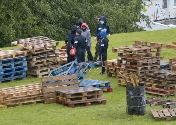 Children, with their faces hidden, construct the controversial Bogside bonfire on the sloped green beneath Londonderry's walls