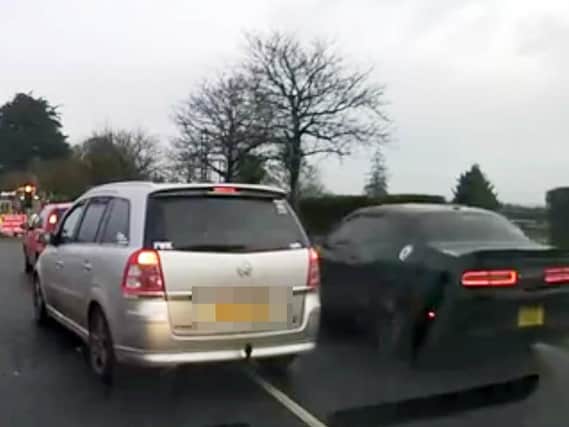 The black car overtakes a line of other vehicles which are all stationary at a red light.